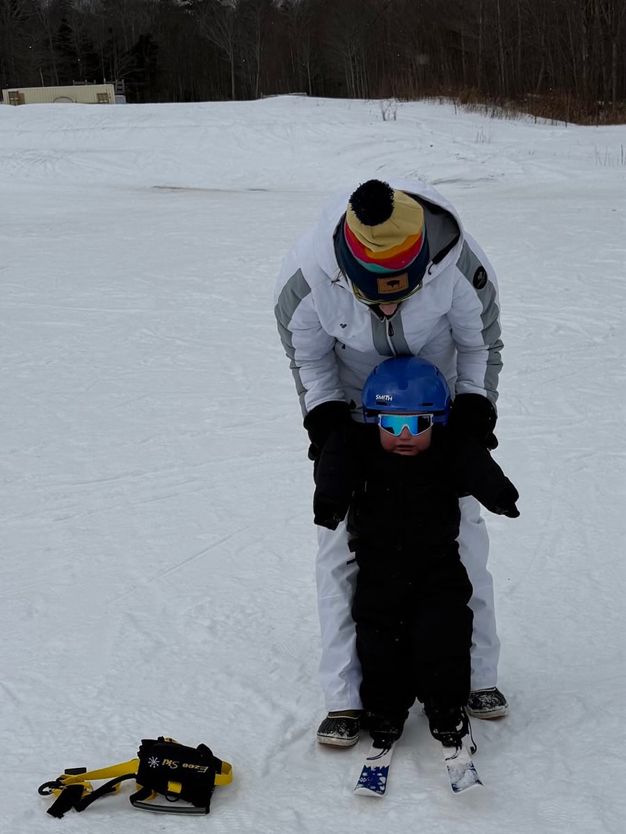 Baby on skis with dad behind him. Baby is wearing Smith Glide Jr. MIPS helmet.