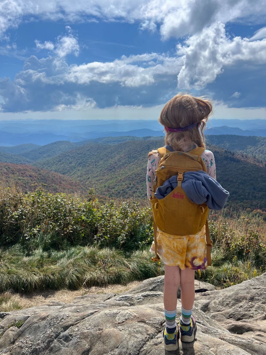 Little girl wearing a yellow tarn 12 backpack at a mountain summit