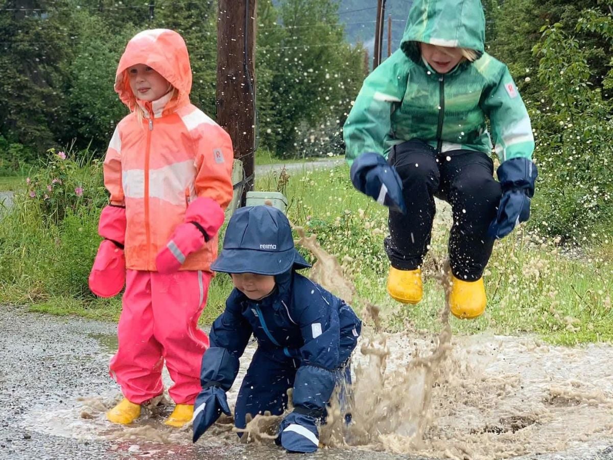 Three kids in the reima rain gear splash in a puddle.