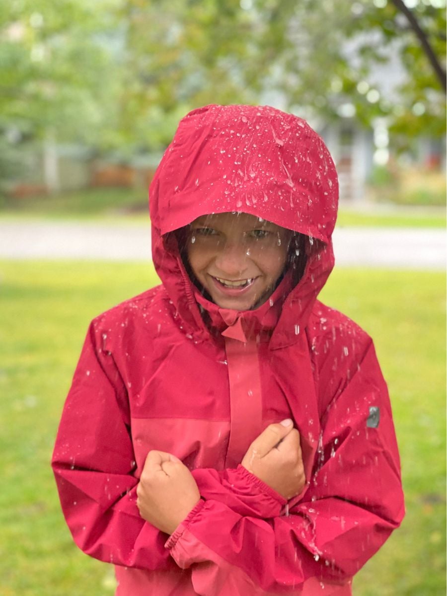 A boy dressed in a rain jacket with rain dripping off.