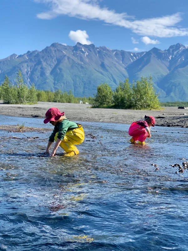 Kids play in a creek wearing rain bibs.