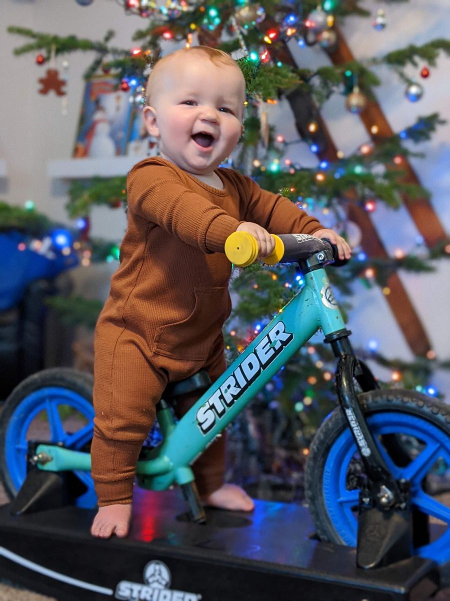 Best indoor active play gifts 3 Baby on a blue strider bike hooked up to a rocking base in front of a Christmas tree
