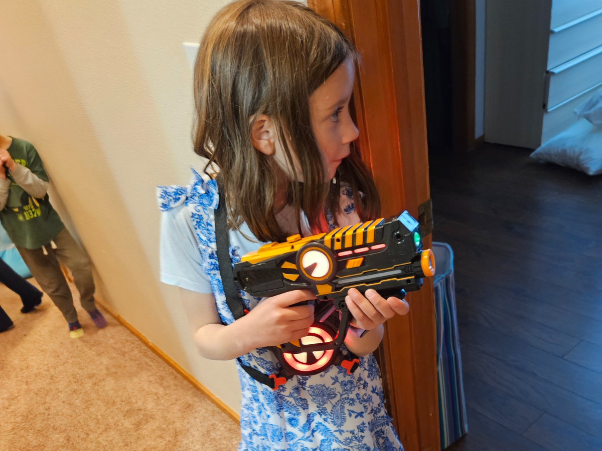 Best indoor active play gifts horizontal 13 Young girl is wearing a light up laser tag vest and is holding a laser tag gun sneaking around a corner.