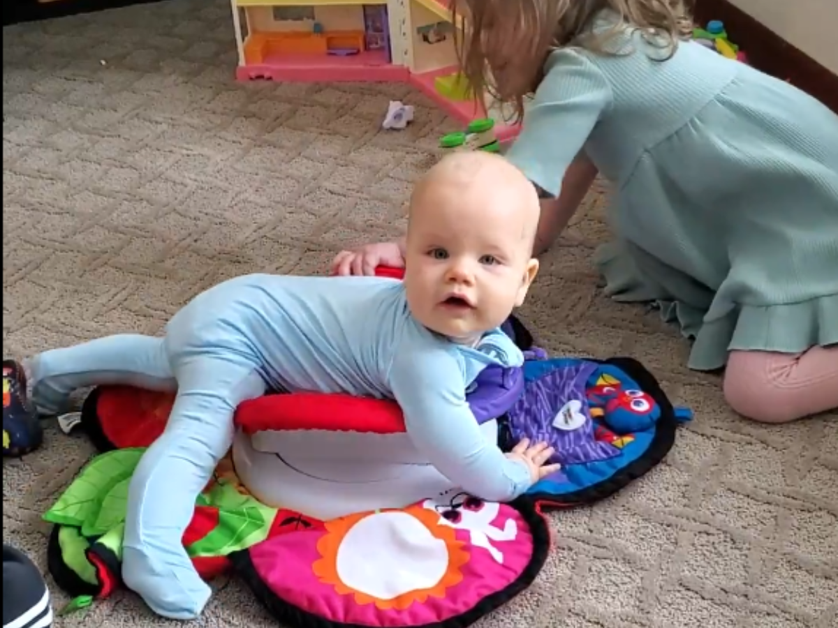 Best indoor active play gifts horizontal 5 Little boy being pushed around by his big sister on a tummy time mat