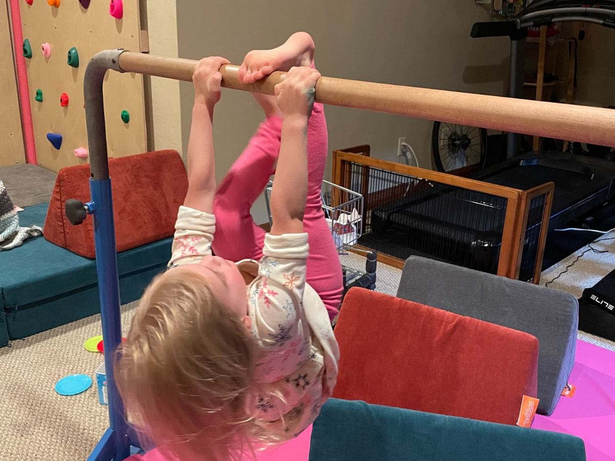 Best indoor active play gifts horizontal 8 Little girl hanging from the gymnastic bar with the nugget couch underneath