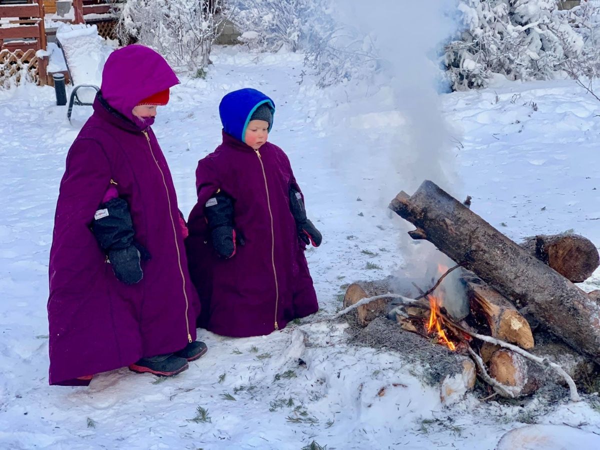 Two kids standing around a winter fire.