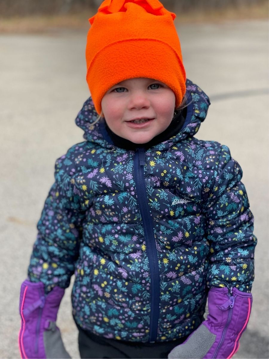 Girl in a bright orange beanie and floral puffy jacket.