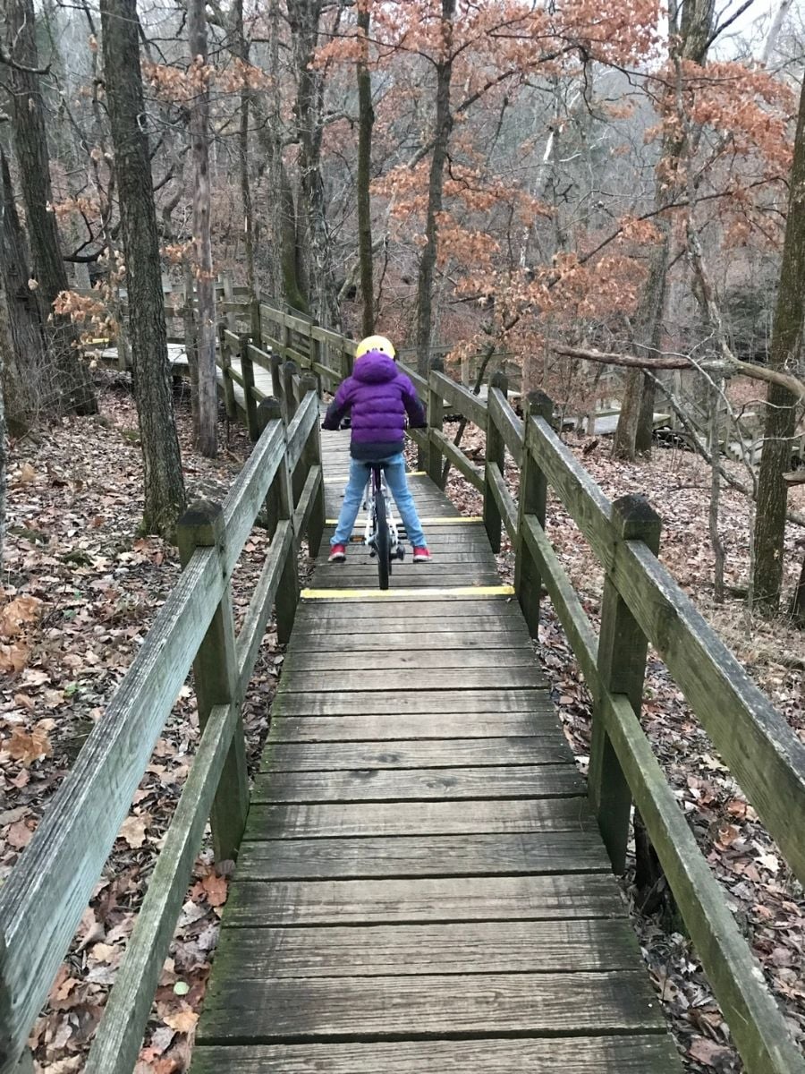 Child riding bike on a wooden bridge wearing a purple puffy jacket.