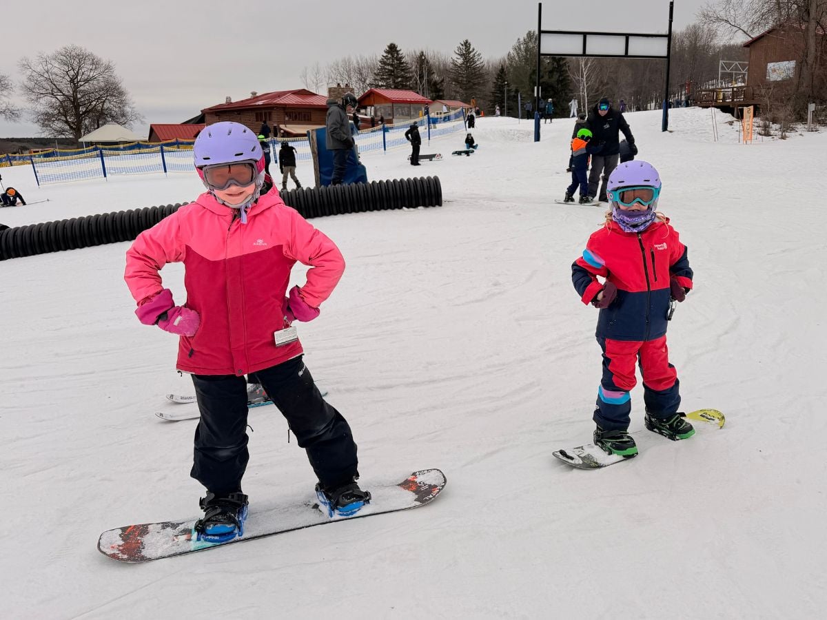 Two girls on snowboards pose for a photo.