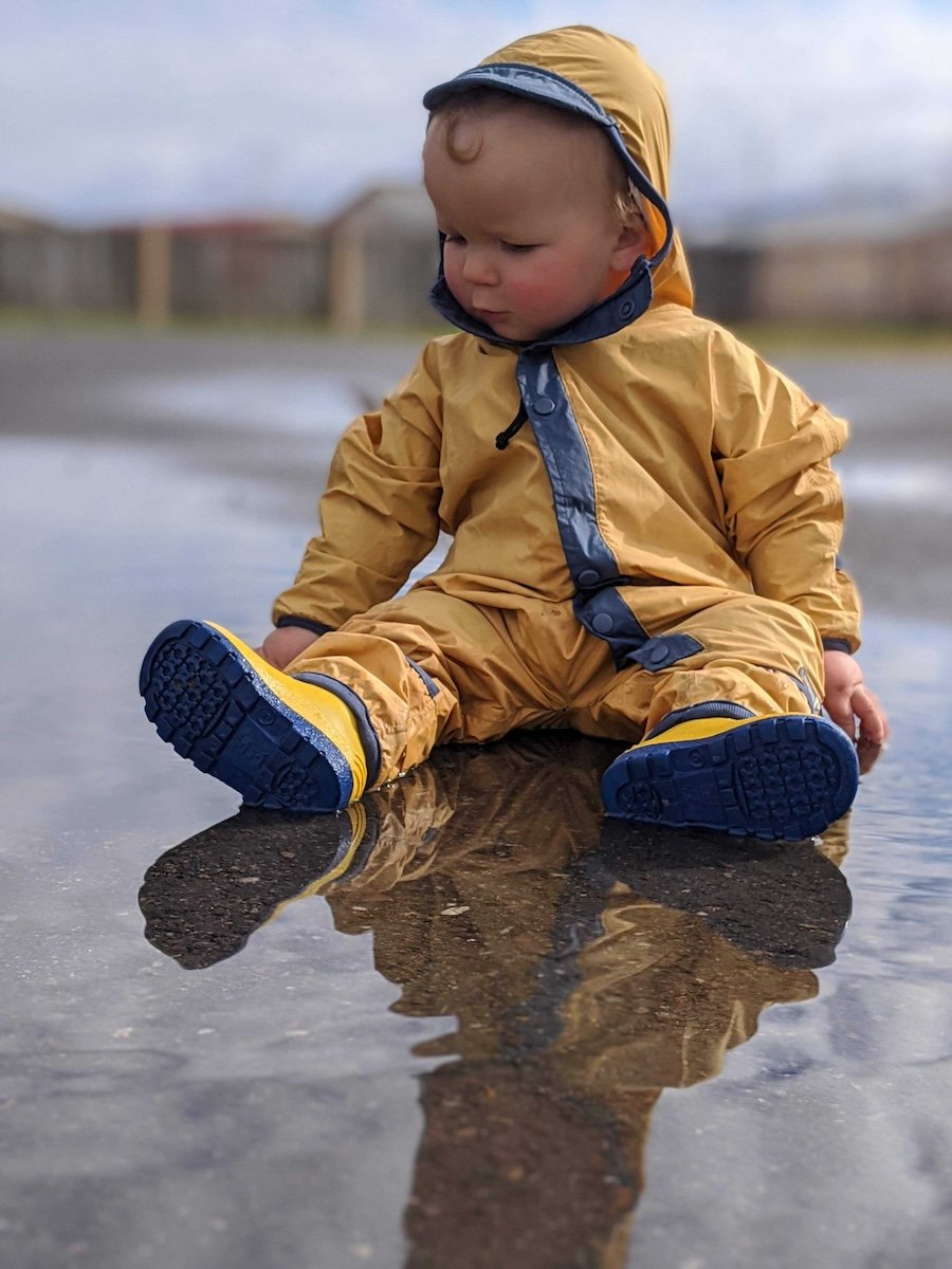 Bestraingearforkids1 boy sitting in the water wearing a rainsuit