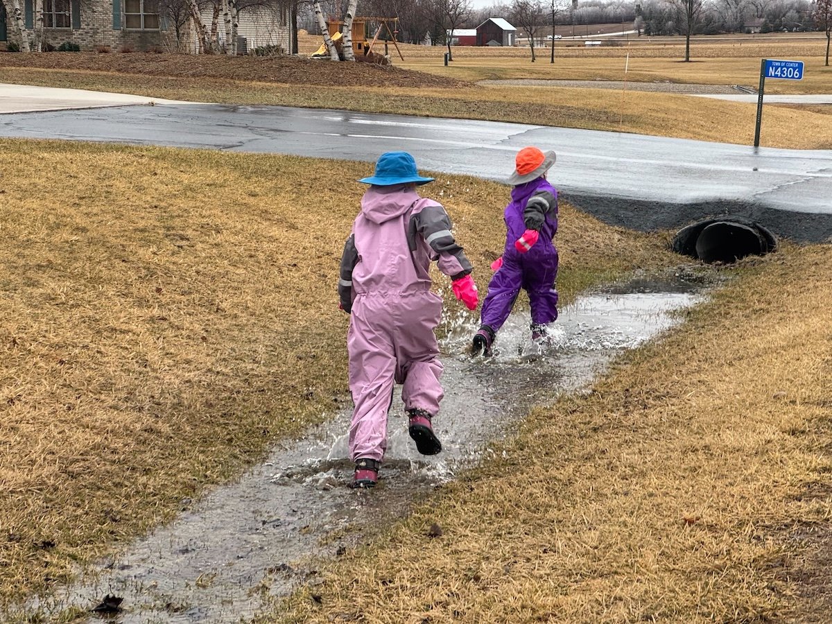 bestraingearforkids5 two girls splashing in a rainy ditch