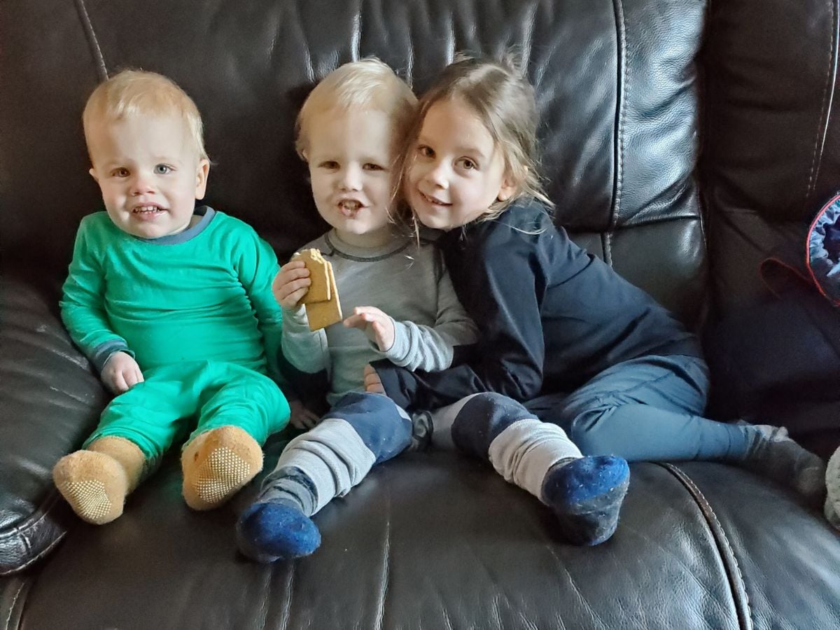 Best Base layers for kids Horizontal -2 Three kids sitting on a couch wearing base layers - Wee Woolies, Helly Hansen, and Akova
