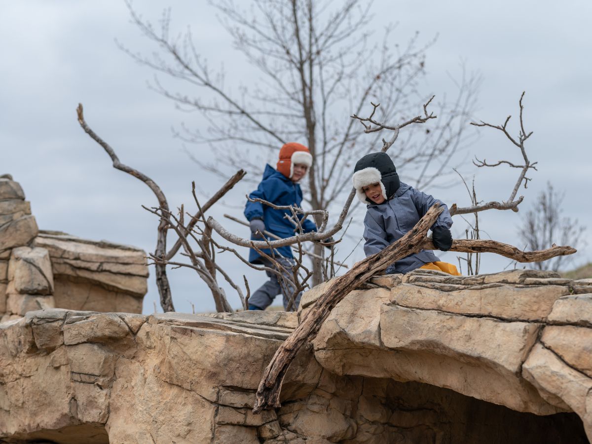 Two boys in trapper hats playing on rocks