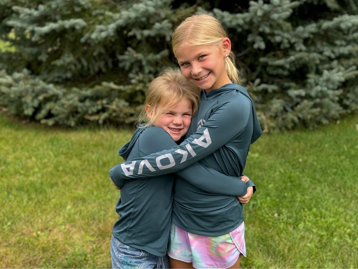 kidsbaselayerakova Two blonde girls hug while wearing Akova longsleeve baselayer top.