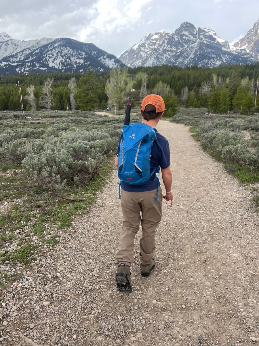 A young man hikes in view of snow-capped mountains, wearing Akova All-Purpose Pants.