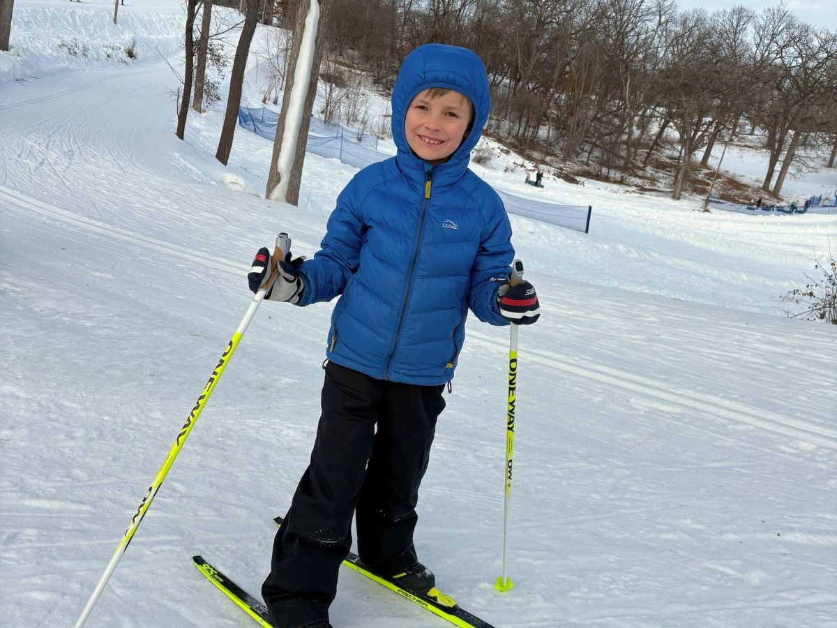 PuffyJacketLifestyle10 A boy in a blue jacket stands on nordic skis.