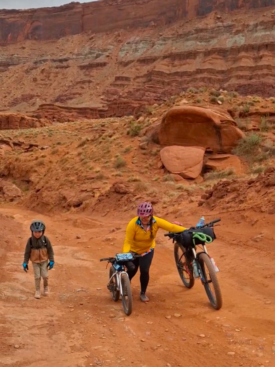 Grit6 A mother pushes her bike and her young son's bike up a hill while bikepacking.