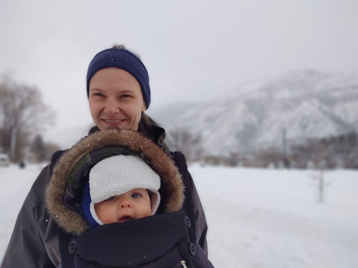 A mother carries a baby in a baby carrier in blowing snow.