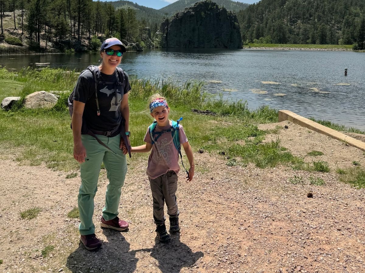 hikingpantsEBFirstAscent A mom and her daughter pose near a lake on a hike.