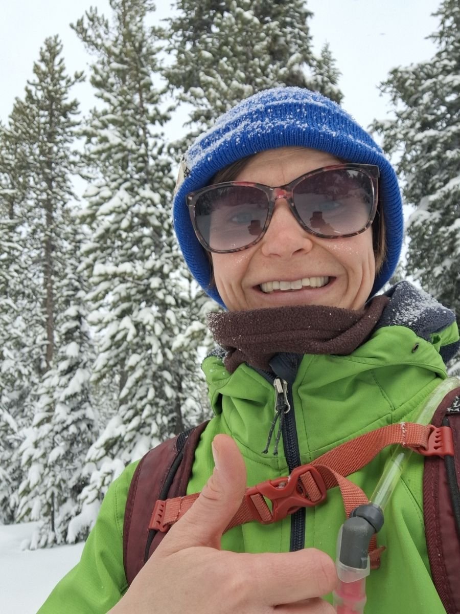 Woman gives a thumbs up while outside in the snow.