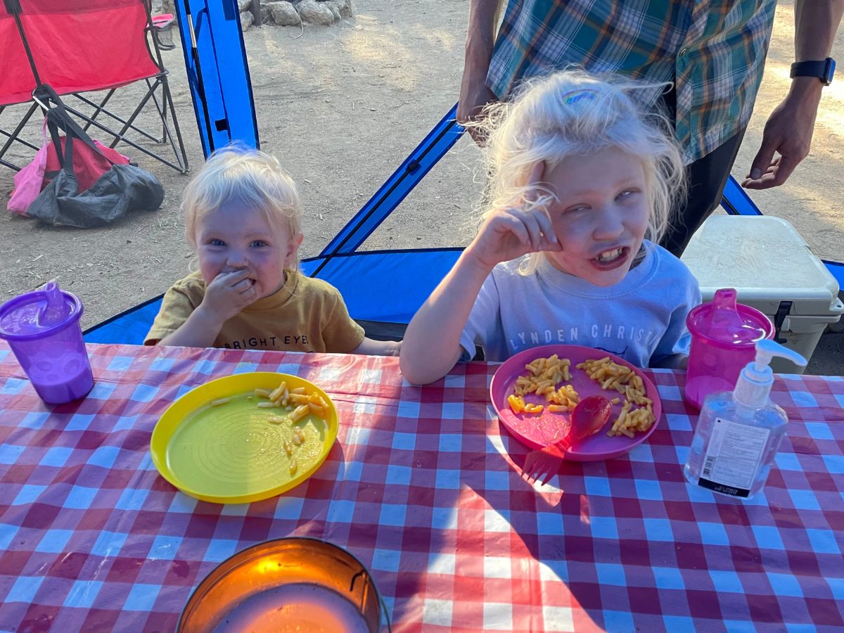 Two kids eating at a picnic table with a checkered tablecloth