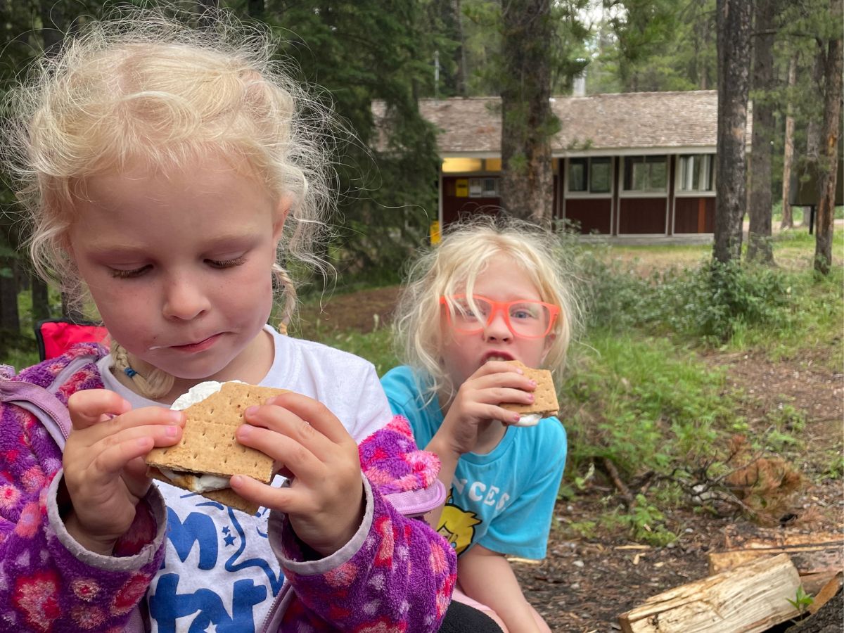 Two girls eating smores with woods in the background