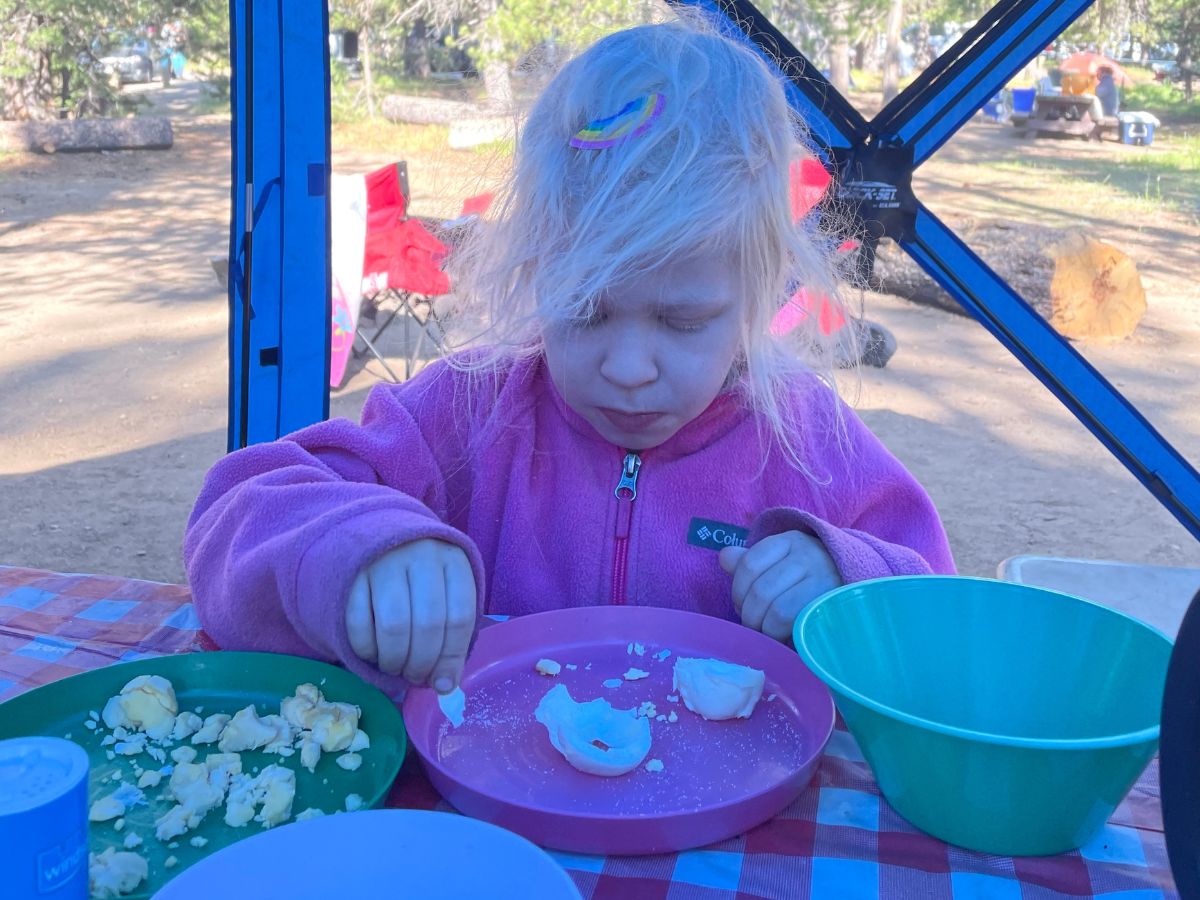 Girl eating hard boiled eggs at a picnic table camping. 