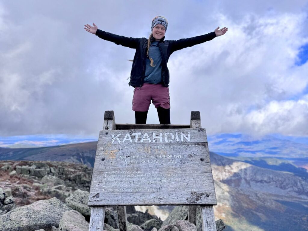 A teenage girl wears the Akova Elevated Ultra Insulated Jacket at the peak of Mount Katahdin in Maine, USA.