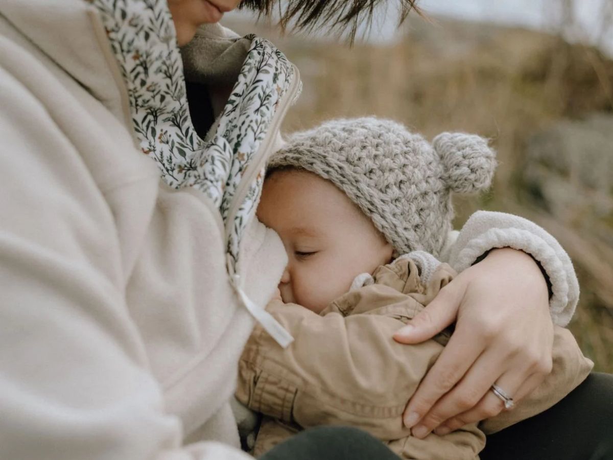 GG_OutdoorWomenLife4 A mother wearing a Wildelore All Phases Fleece nurses her baby outdoors.