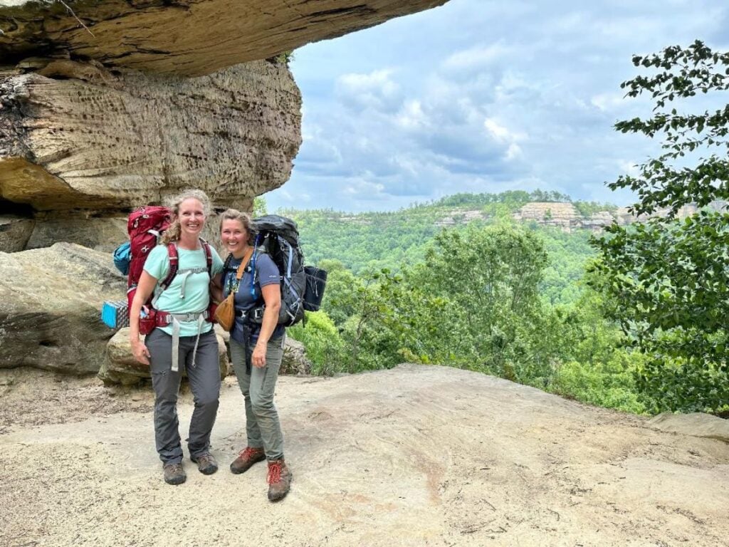 Two women wear hiking gear in an area with multiple rock formations.