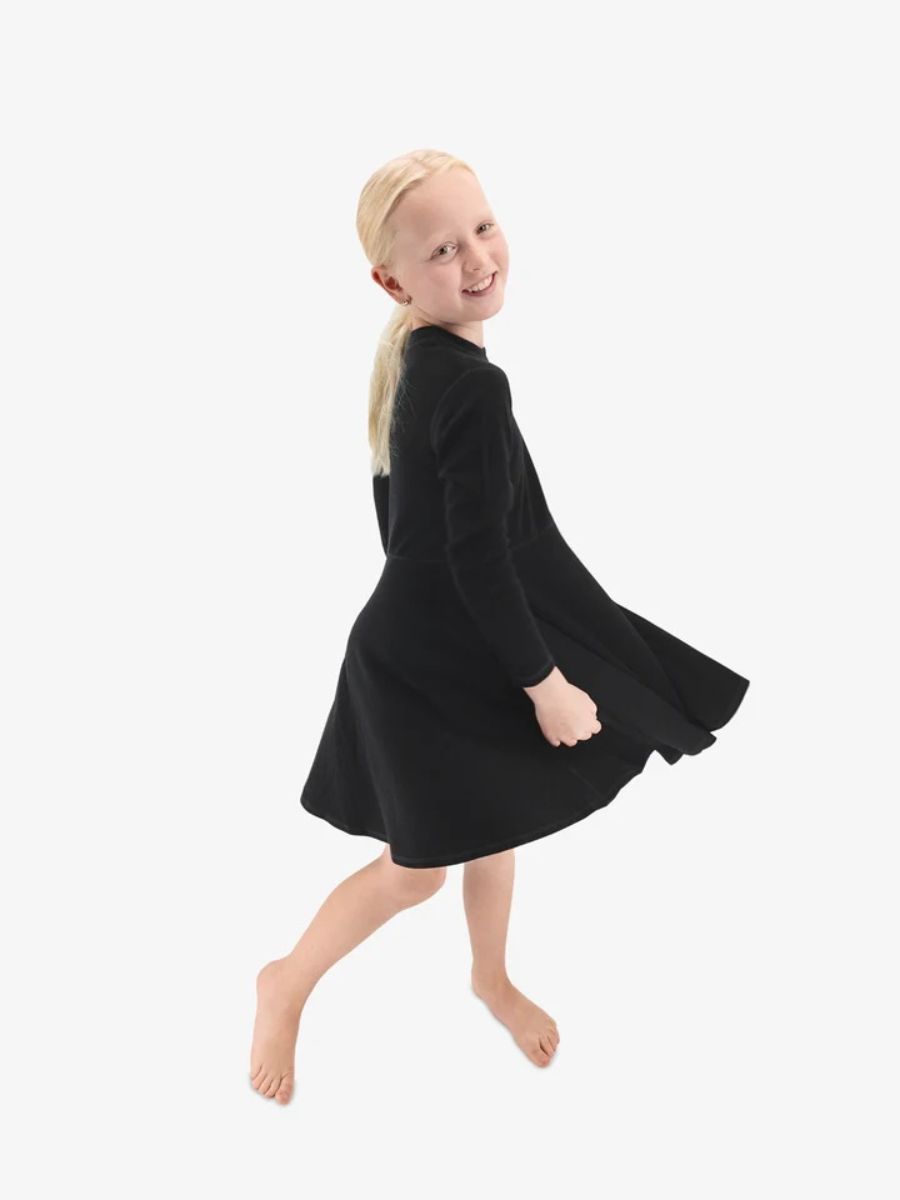 WomenOwnedGear_IksplorDress A girl model in a black long-sleeved twirls and smiles at the camera