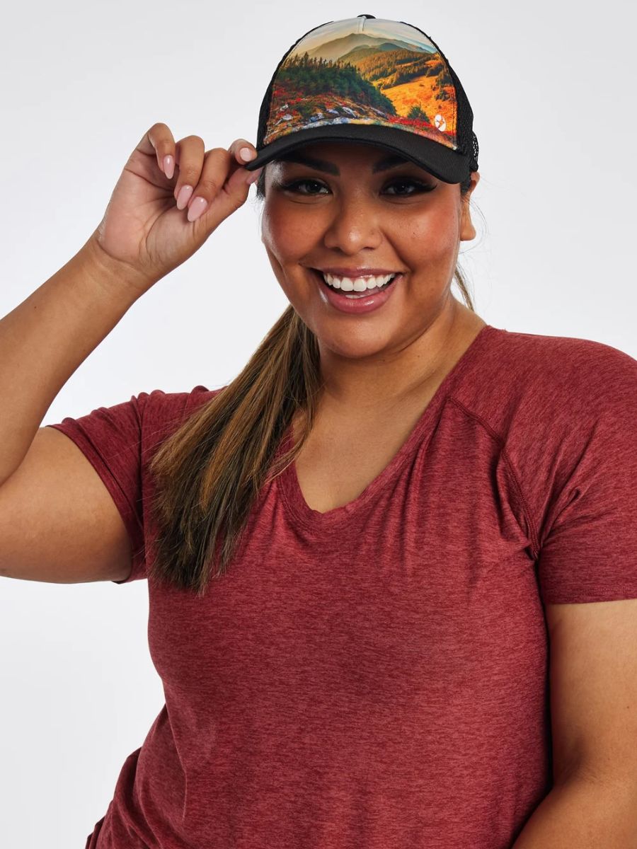 A model wears a hat with mountains on it and a maroon shirt.