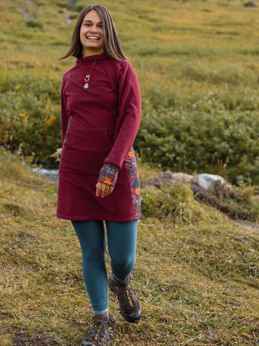 A woman in a maroon dress smiles at the camera, she's outside in a field