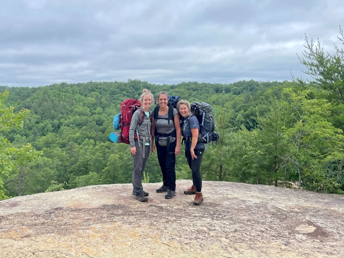3 female backpackers stand on a rock overlook.