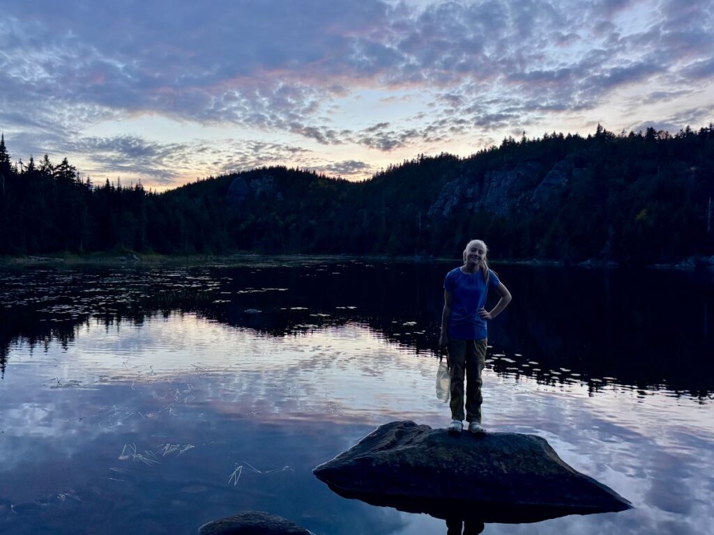 A teenage girl gathers water at a pond.
