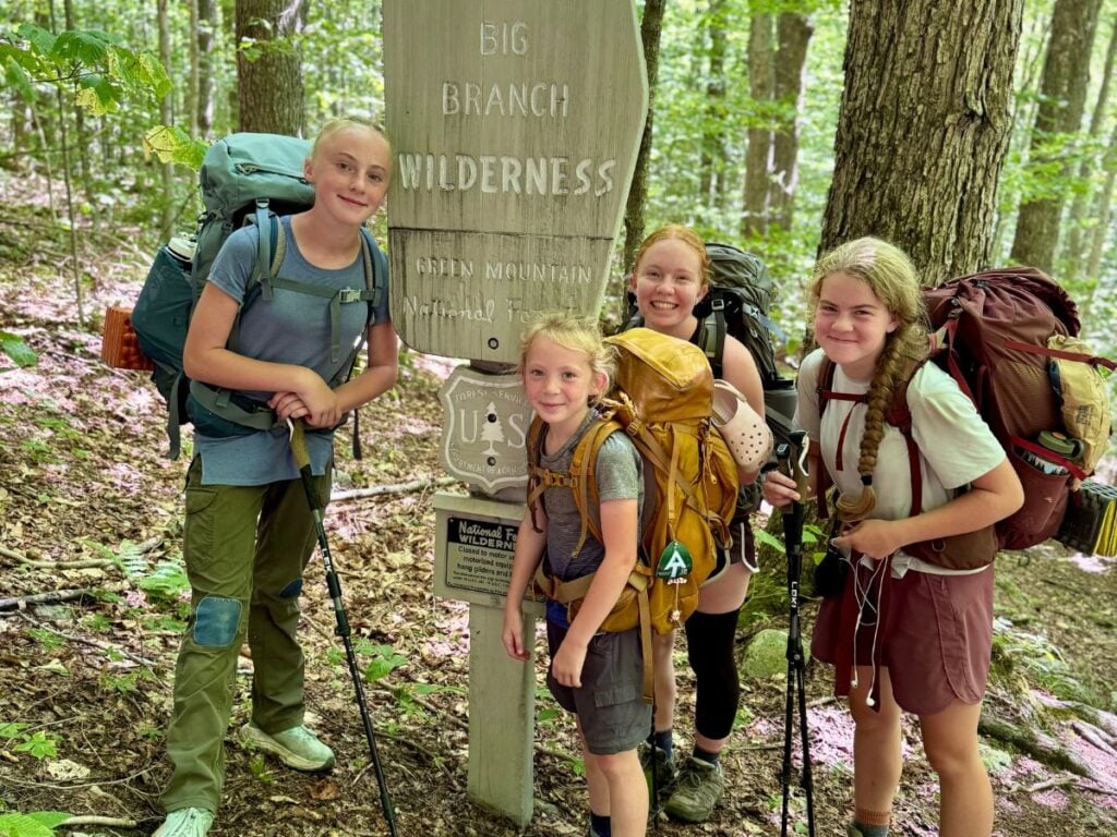 Four sisters stand near a sign for the Big Branch Wilderness in the Green Mountain National Forest.