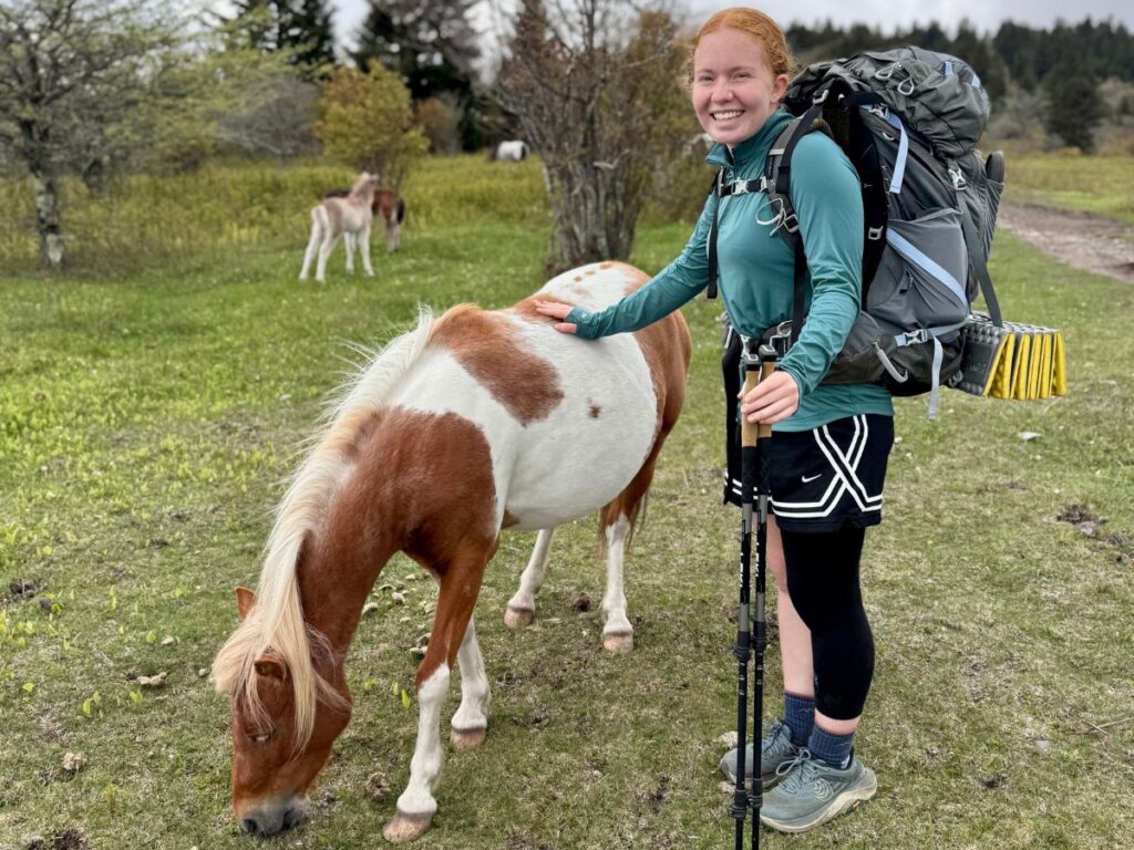 A teenage girl poses next to a miniature horse.