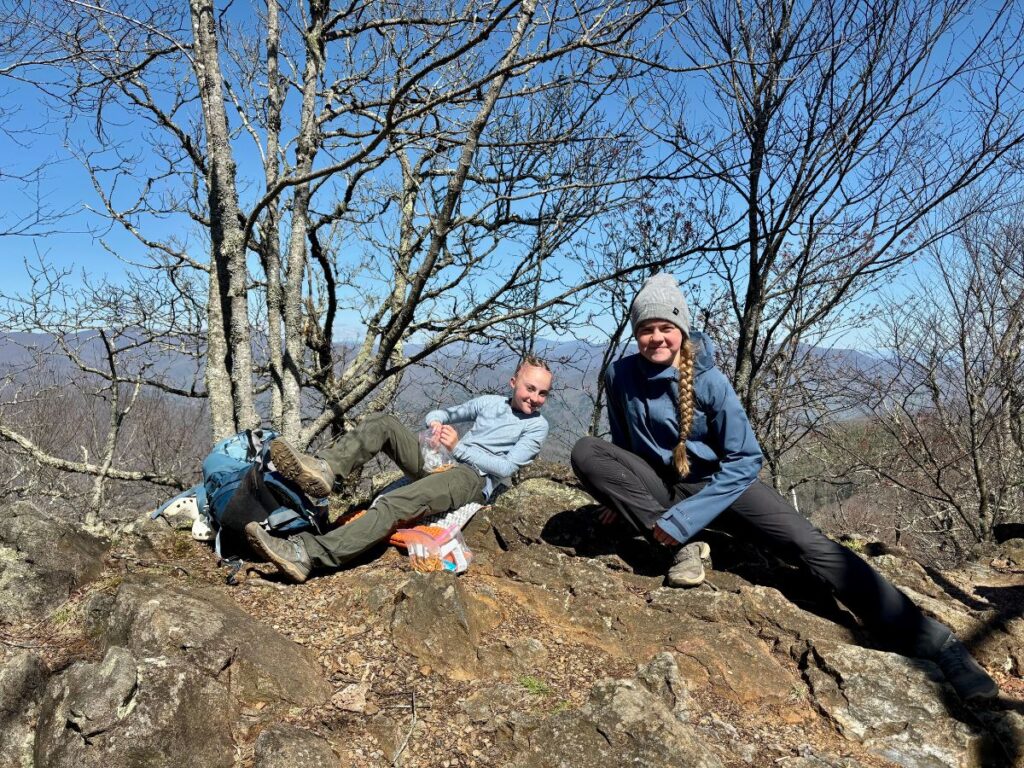 Two teenage girls take a snack break in the woods.