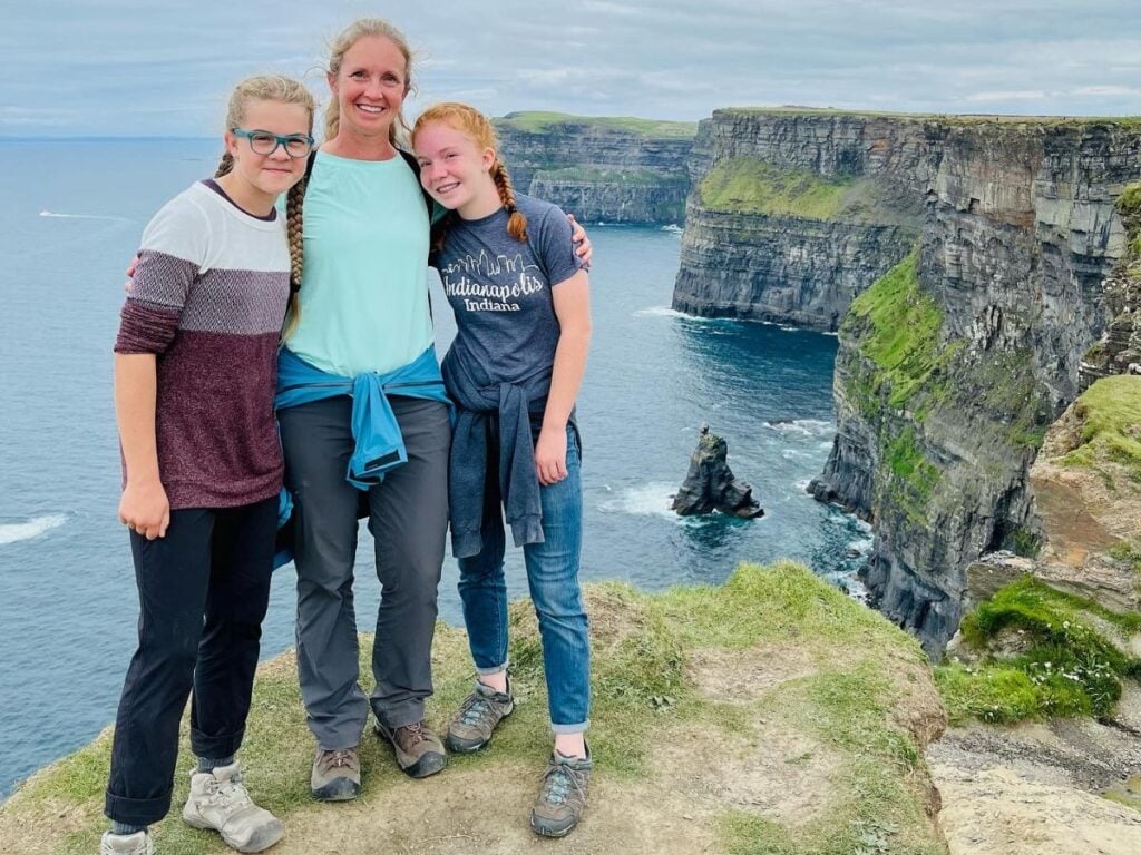 A mom and two teenage girls pose near the Cliffs of Moher in Ireland.