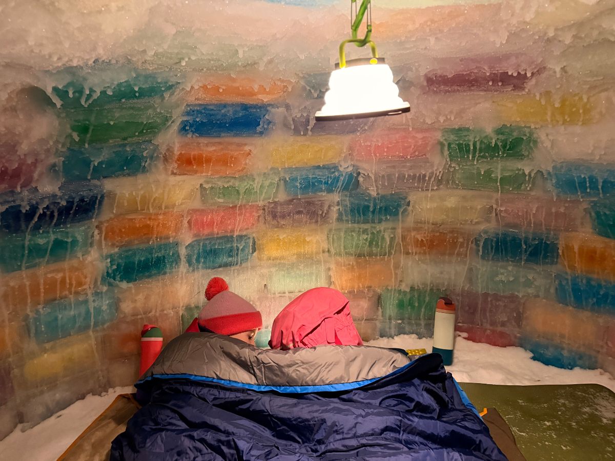 Buildaniceigloo14 Two kids snuggle in a sleeping bag a read in a colored ice block igloo.