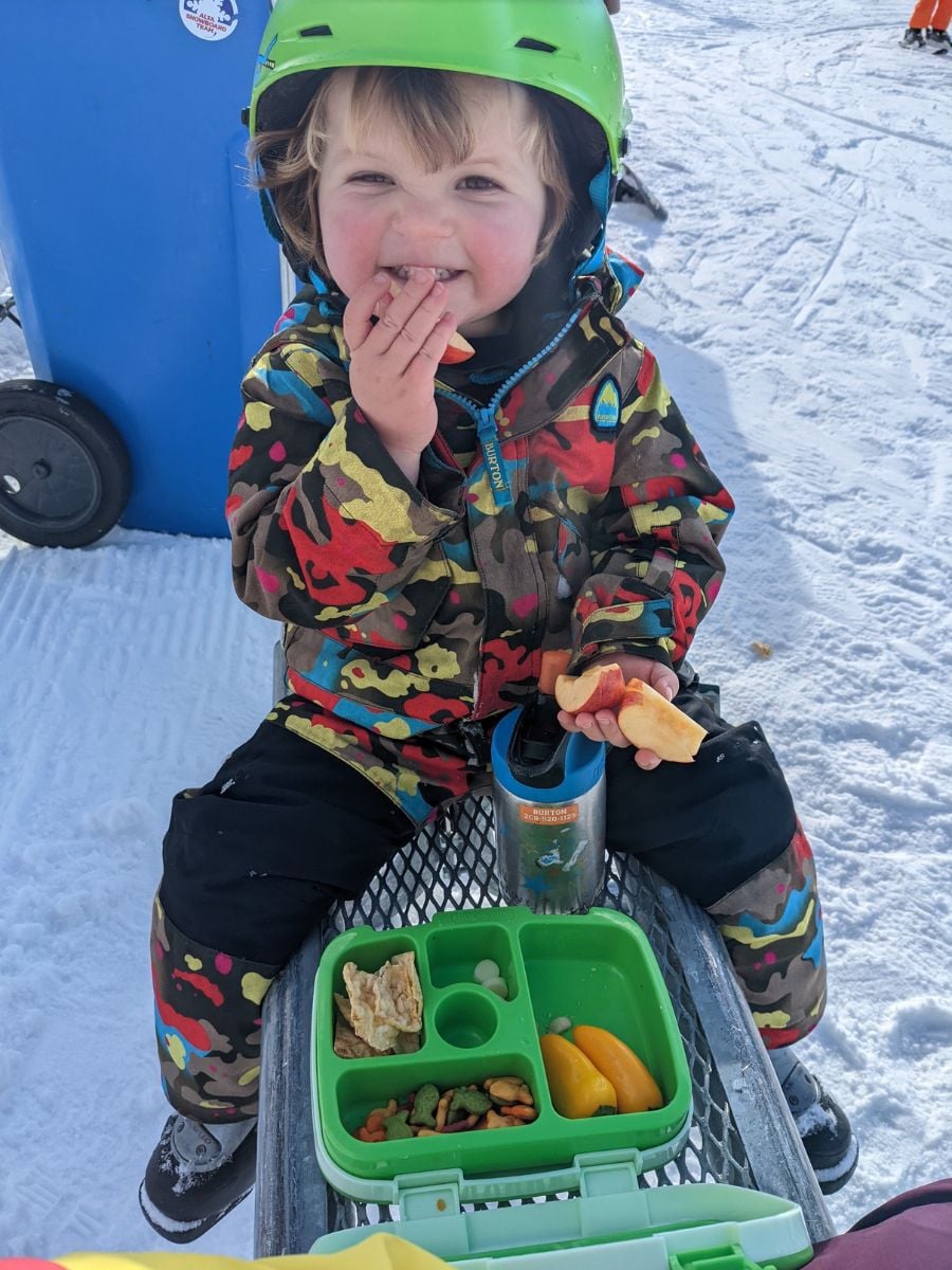 SkiFood1 A child eats from his lunch box outside in winter.
