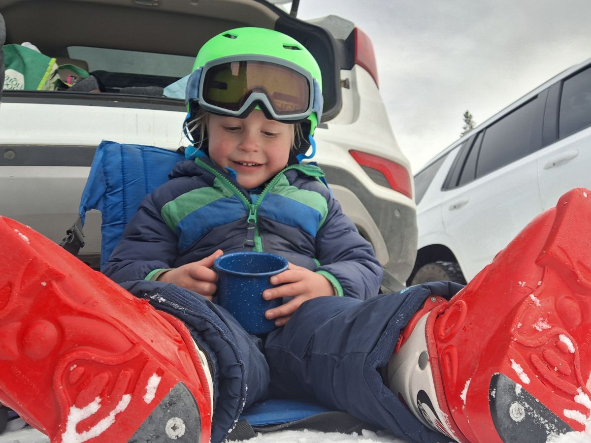 A child drinks a cup of hot chocolate during a break from skiing.