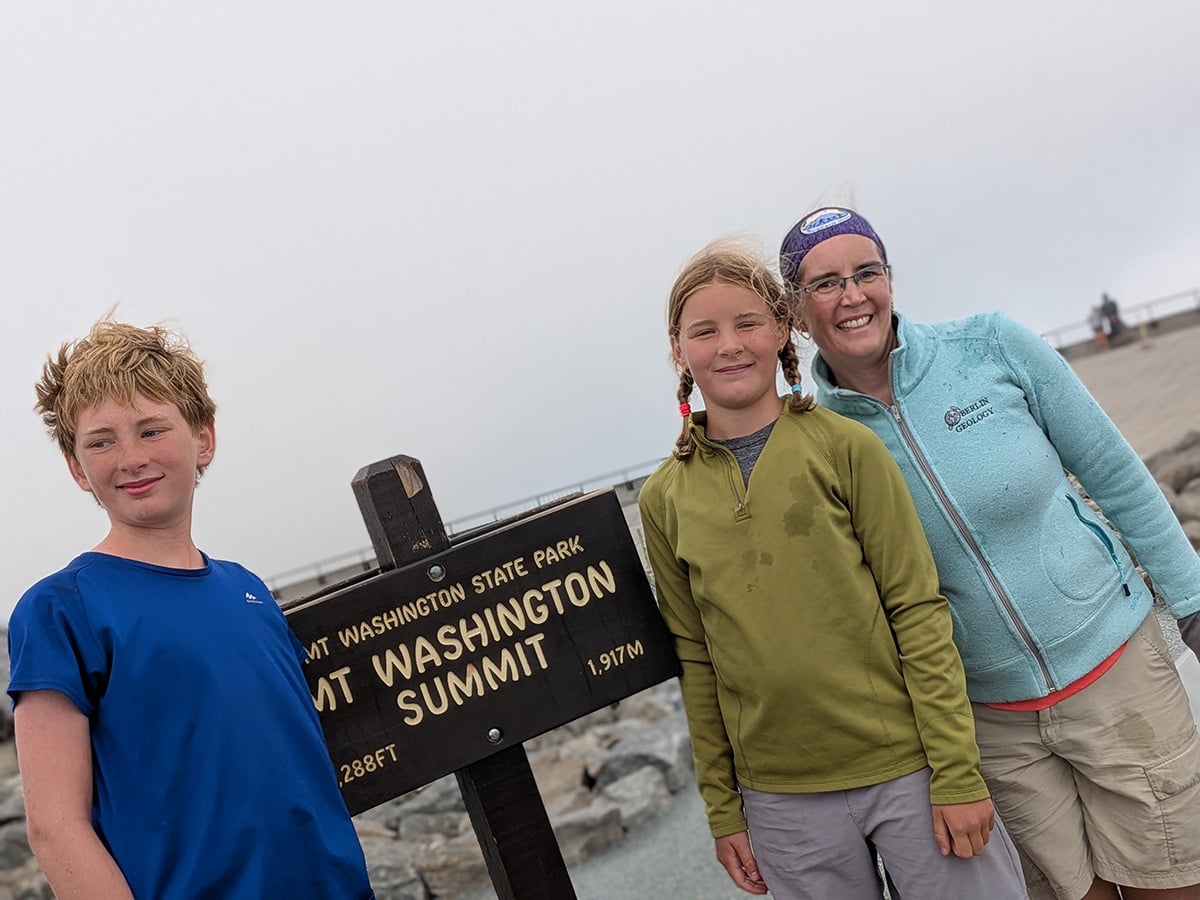 Mother and two children next to a Mount Washington sign on the summit.