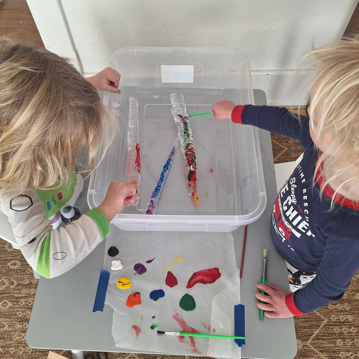 Two children painting icicles in a bin.