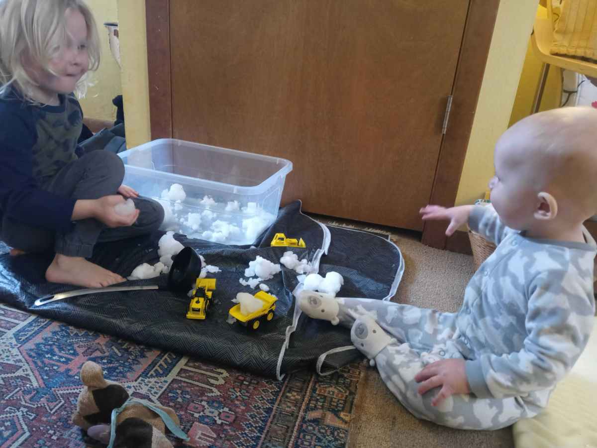 two children playing with toy trucks filled with snow.