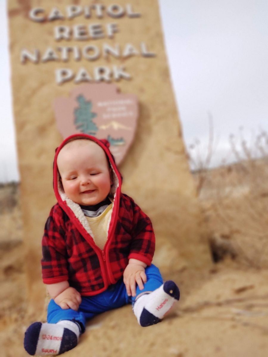 NtlParks6 A baby sits in front of a sign for Capitol Reef National Park.