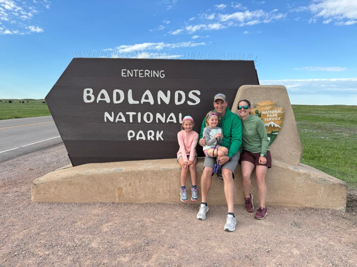 A family sits together at the Badlands National Park sign.