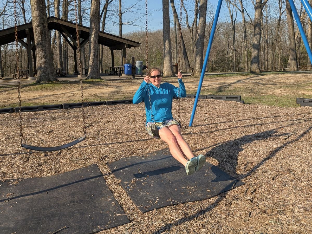 t9sunandswim_4 A woman with a bright blue sun shirt swings on a swing set.