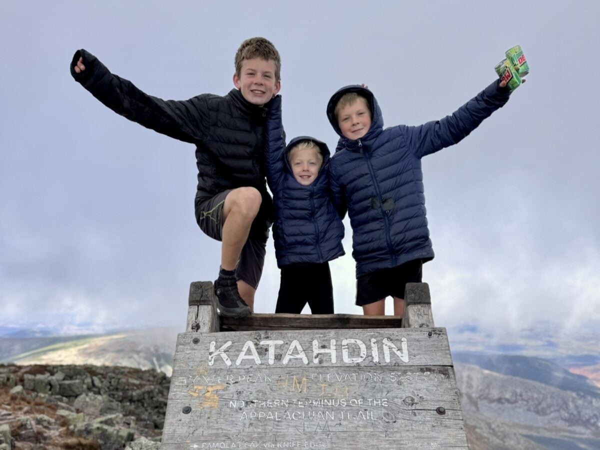 Three young brothers pose atop the Appalachian Trail Northern Terminus sign on Mount Katahdin.