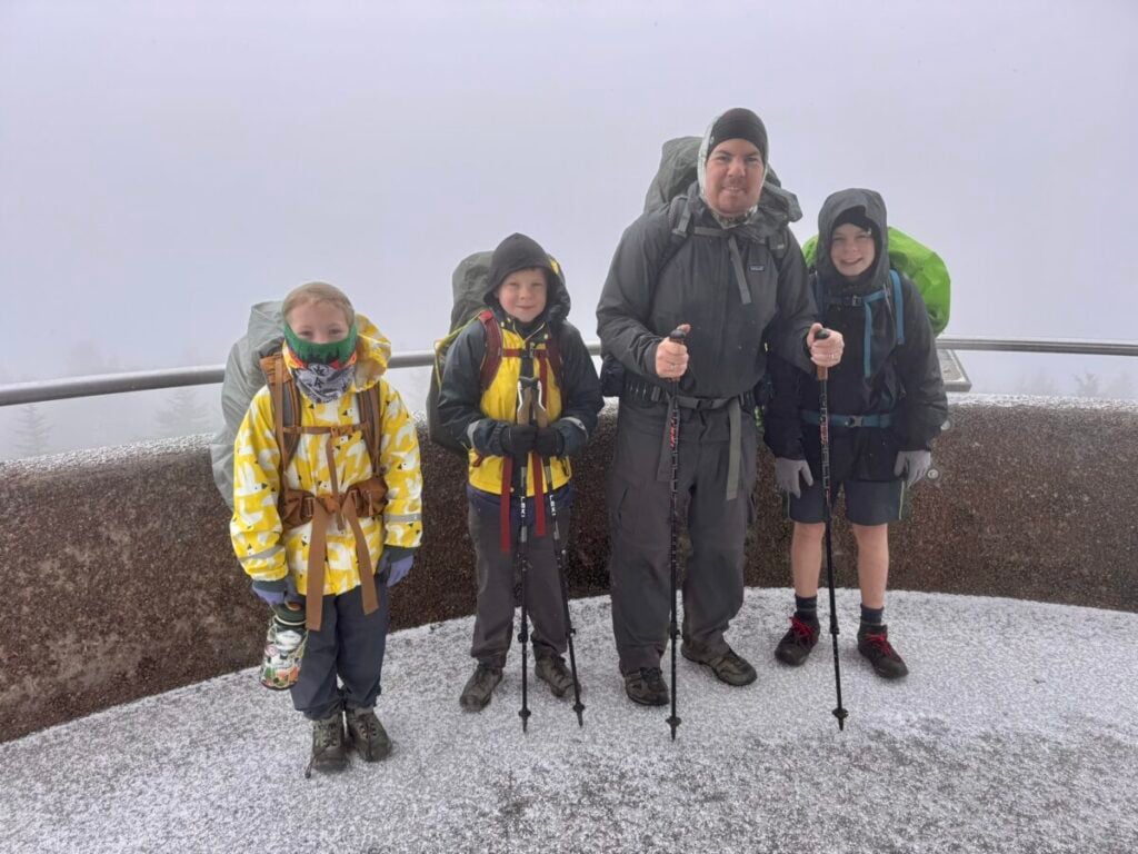 A father with three children stand atop the Kuwohi tower, wearing cold weather gear, with snow on the ground around them.